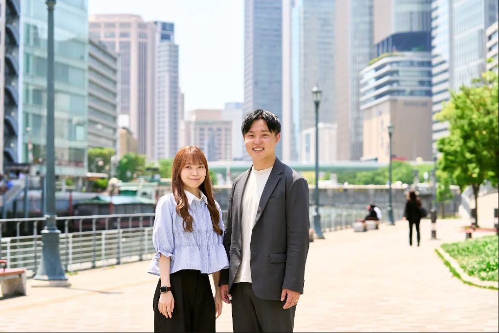 大阪の街を背景に立つmum.realestateの夫婦ふたり